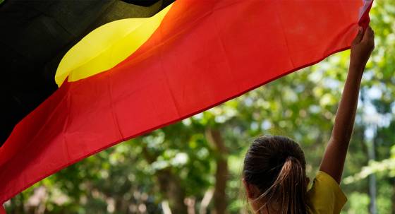 A young girl holds an Aboriginal flag (Image: AAP/Rick Rycroft)