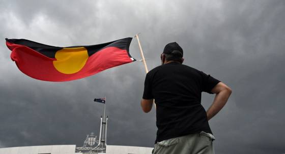A man holds the Aboriginal flag outside Parliament House (Image: AAP/Mick Tsikas)